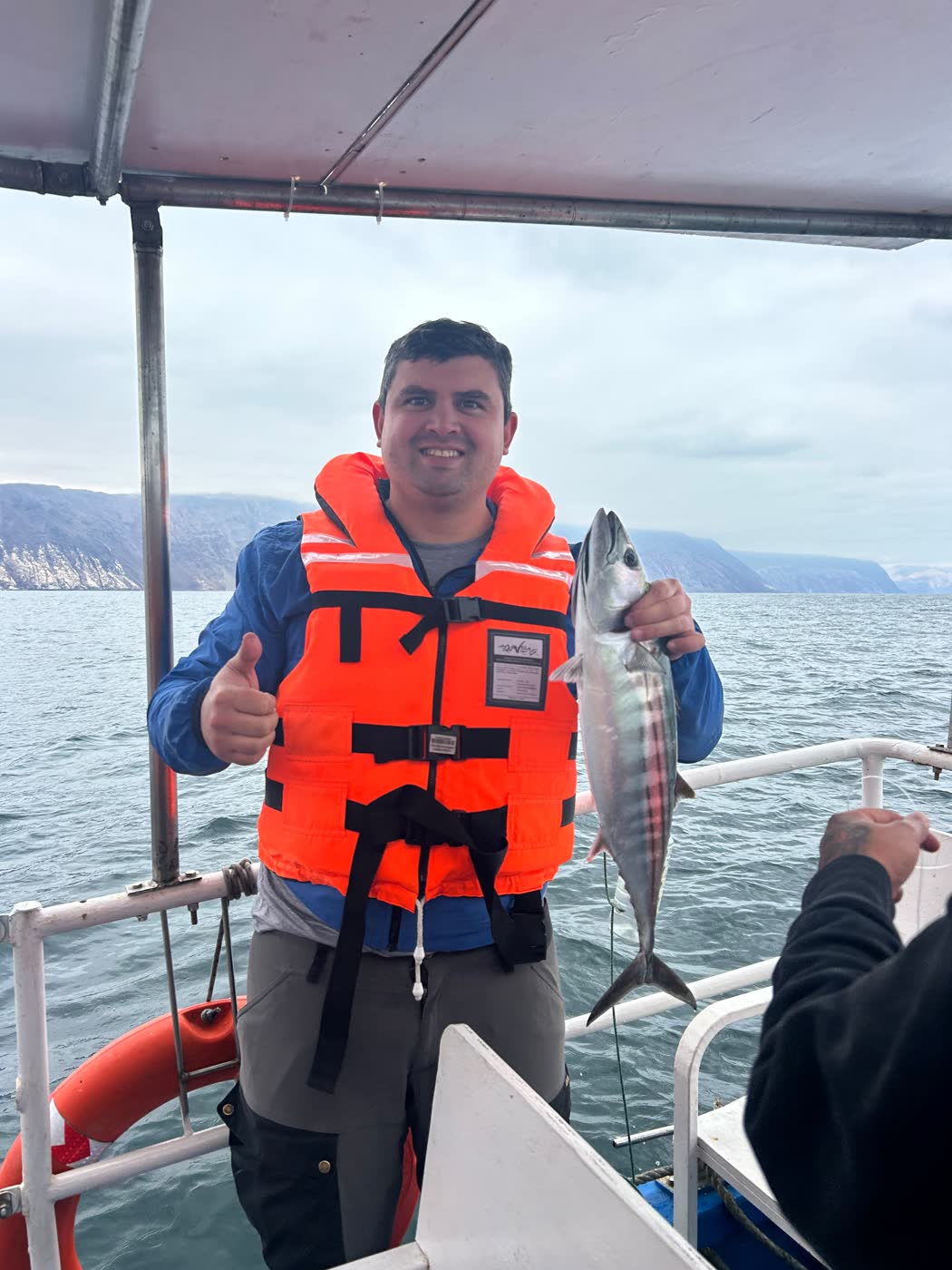 Pasajero mostrando su captura a bordo, con los acantilados de Arica de fondo